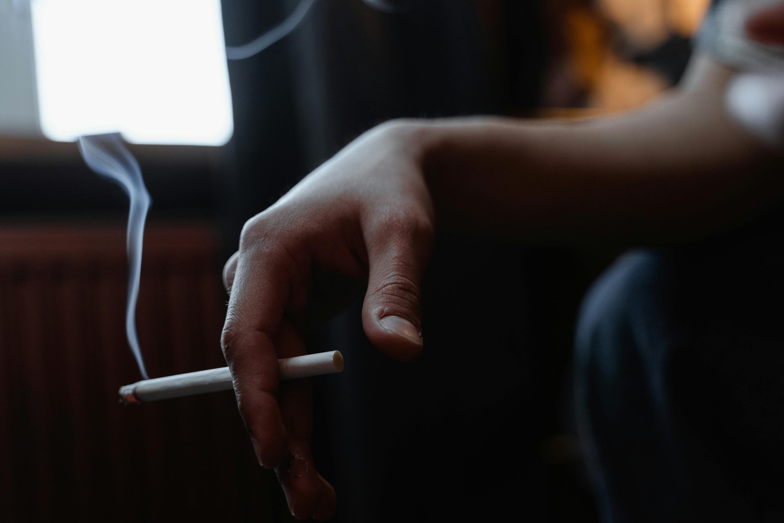 Man's hand resting on his knee, holding a smoldering cigarette